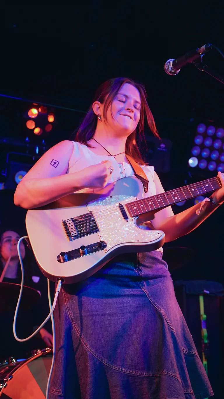 claudia fenoglio plays a white electric guitar on stage