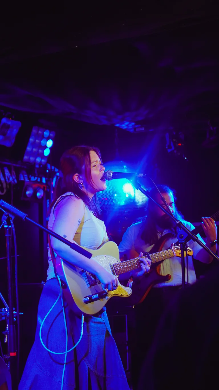 claudia fenoglio plays a white electric guitar on stage