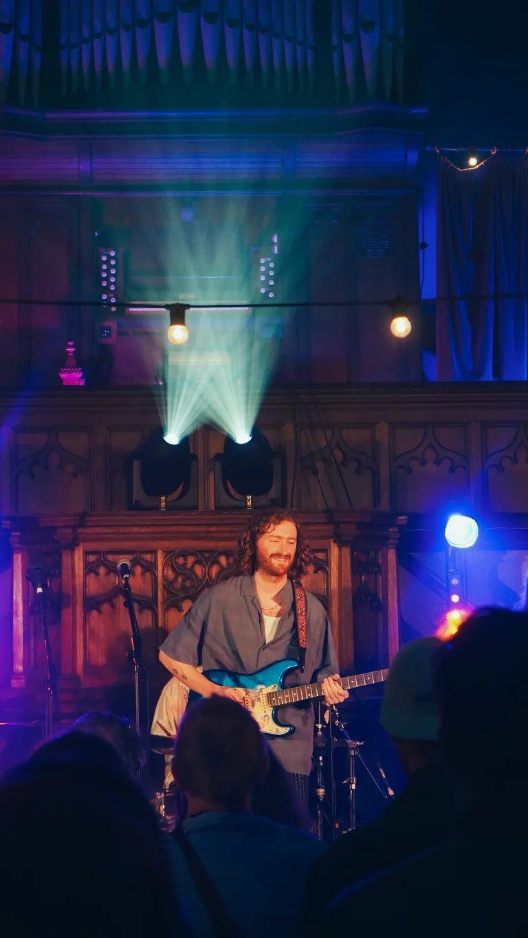 george bloomfield performs on stage, holding a blue electric guitar