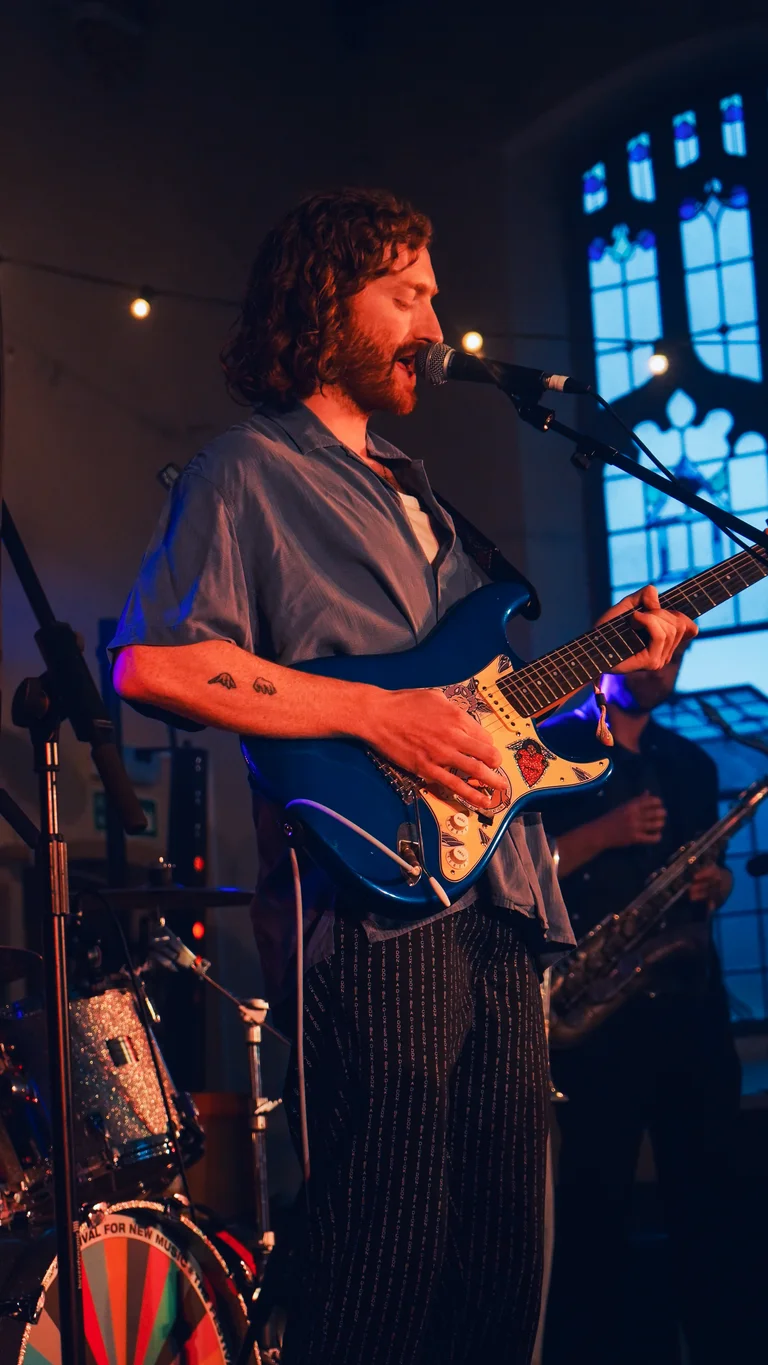 george bloomfield performs on stage, holding a blue electric guitar