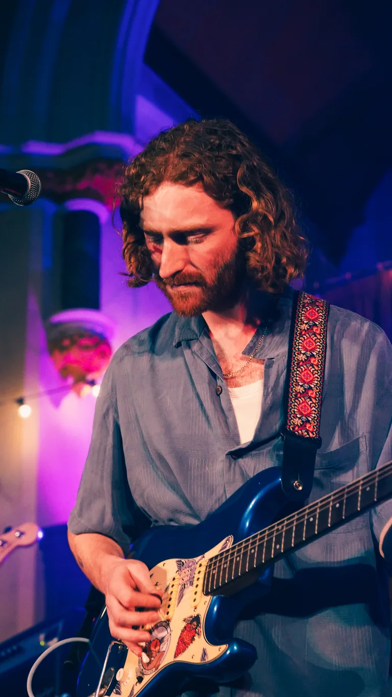 george bloomfield performs on stage, holding a blue electric guitar
