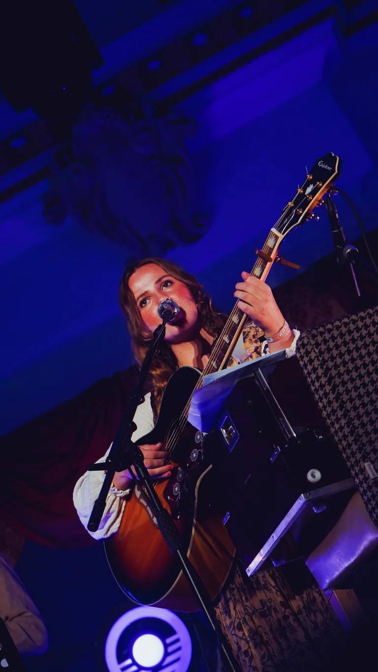 mari mathias holds her guitar and sings on stage