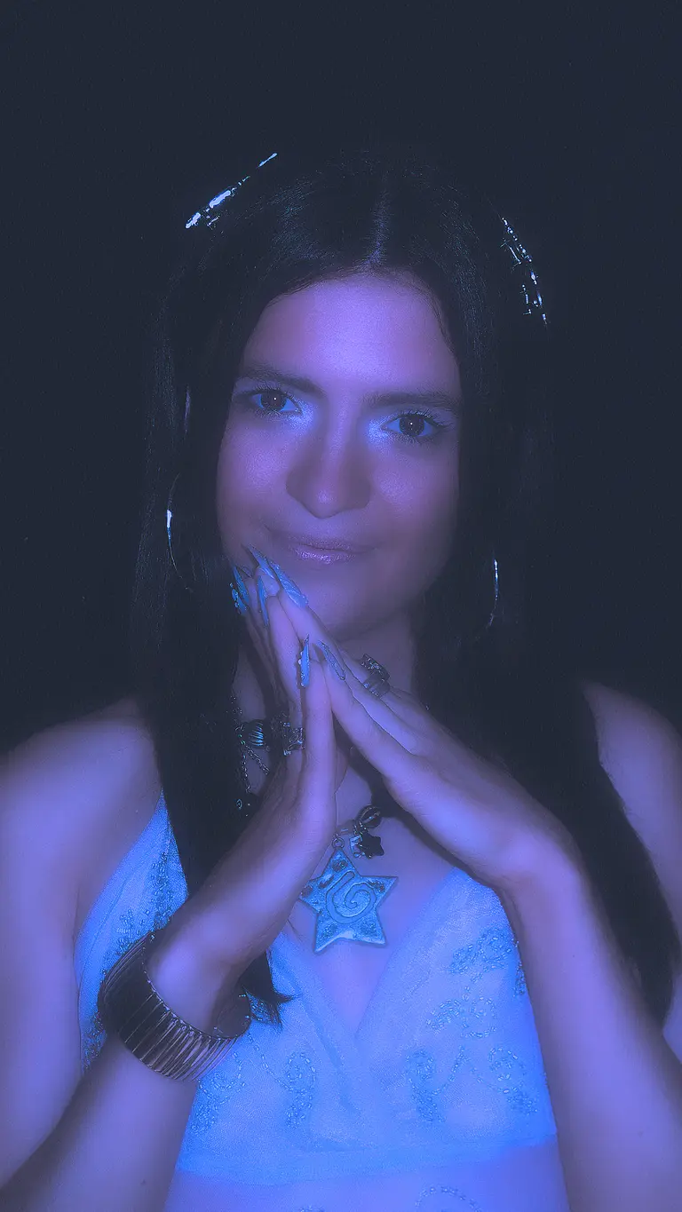 melba holds her hands together by her chin. her eyes are traced in a shimmery blue