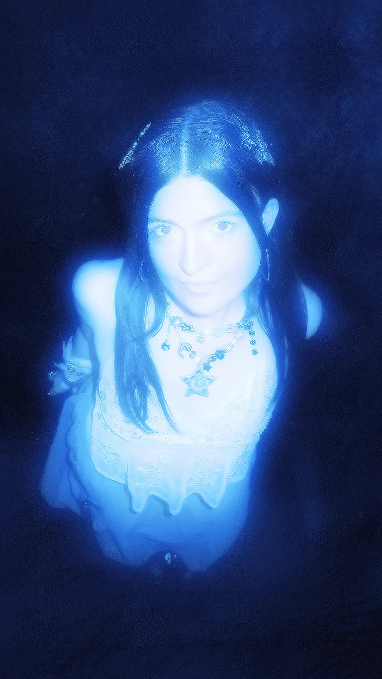 melba is illuminated in an ethereal blue light; she looks at the camera