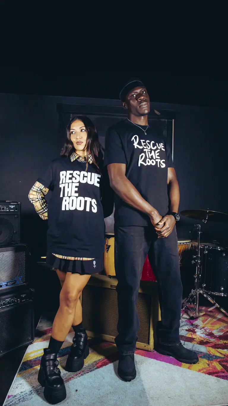 lockdownT and Jess Iszatt stating up ion a stage wearing two black t-shirts with the Rescue the Roots handwritten logo 