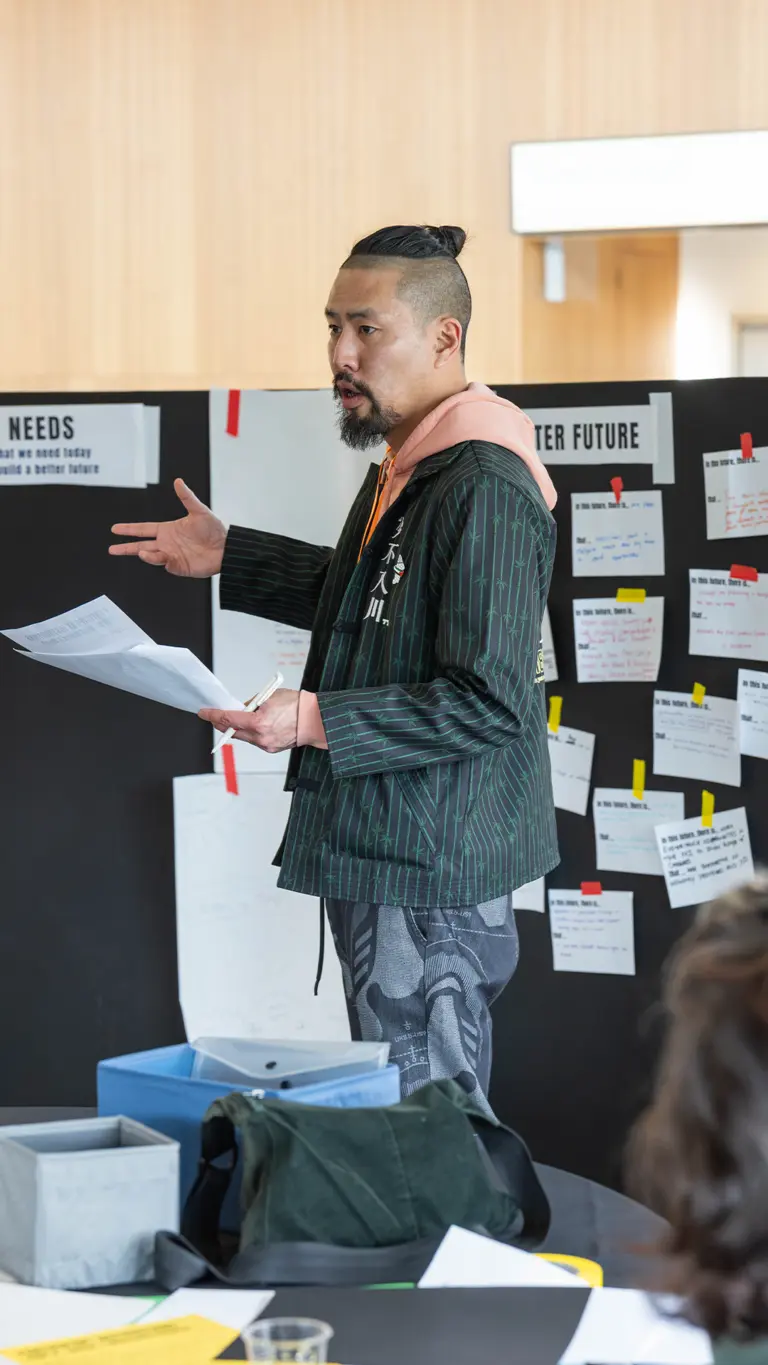 a man stands up, holds paper and talks to a room