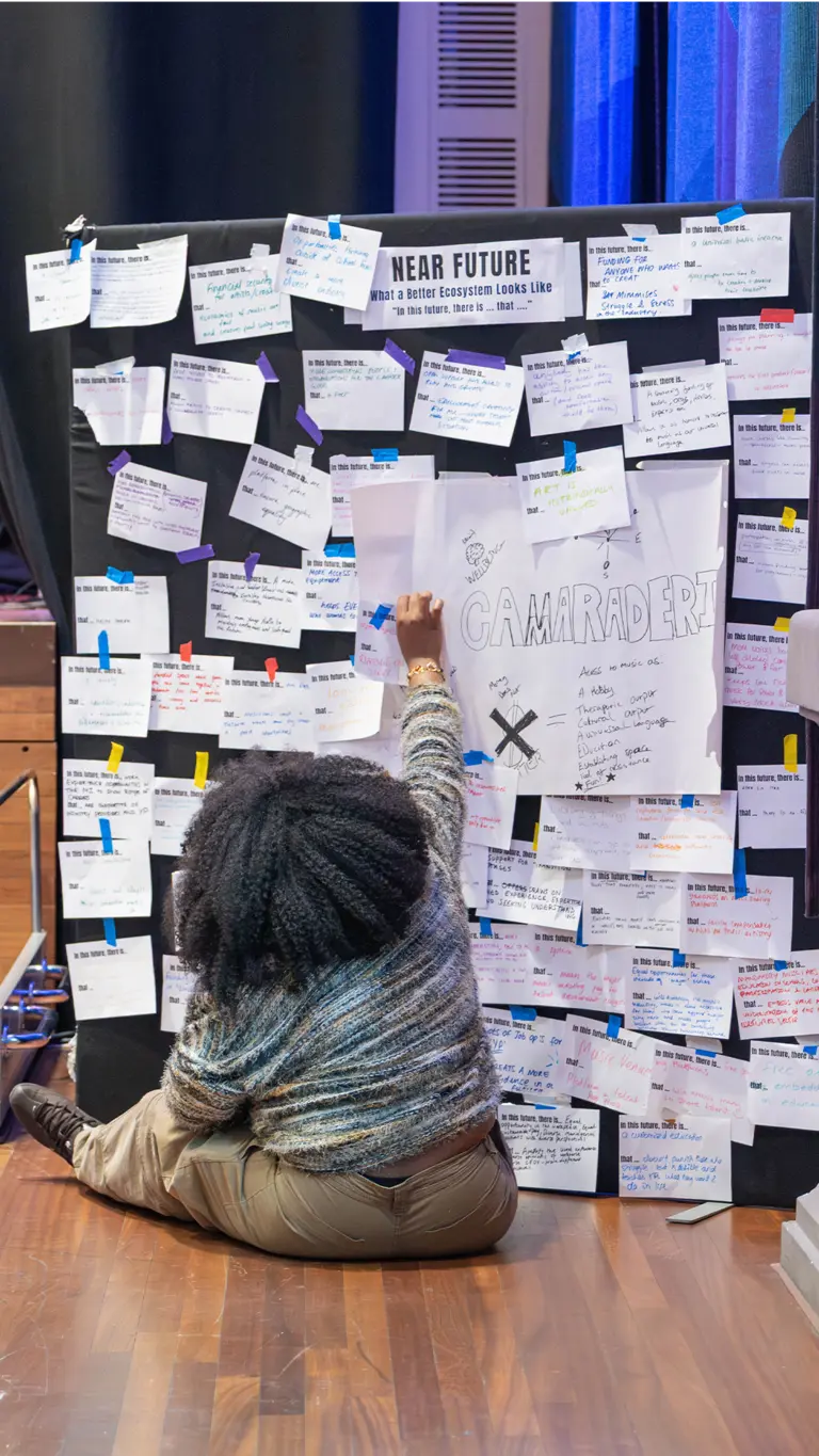 a woman sits on the floor and reaches up to a board full of pinned notes
