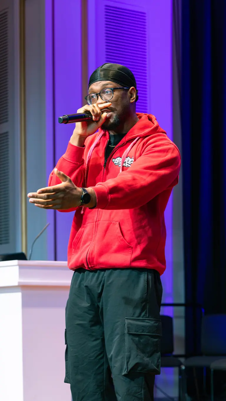 a man in a red hoodie raps into a microphone