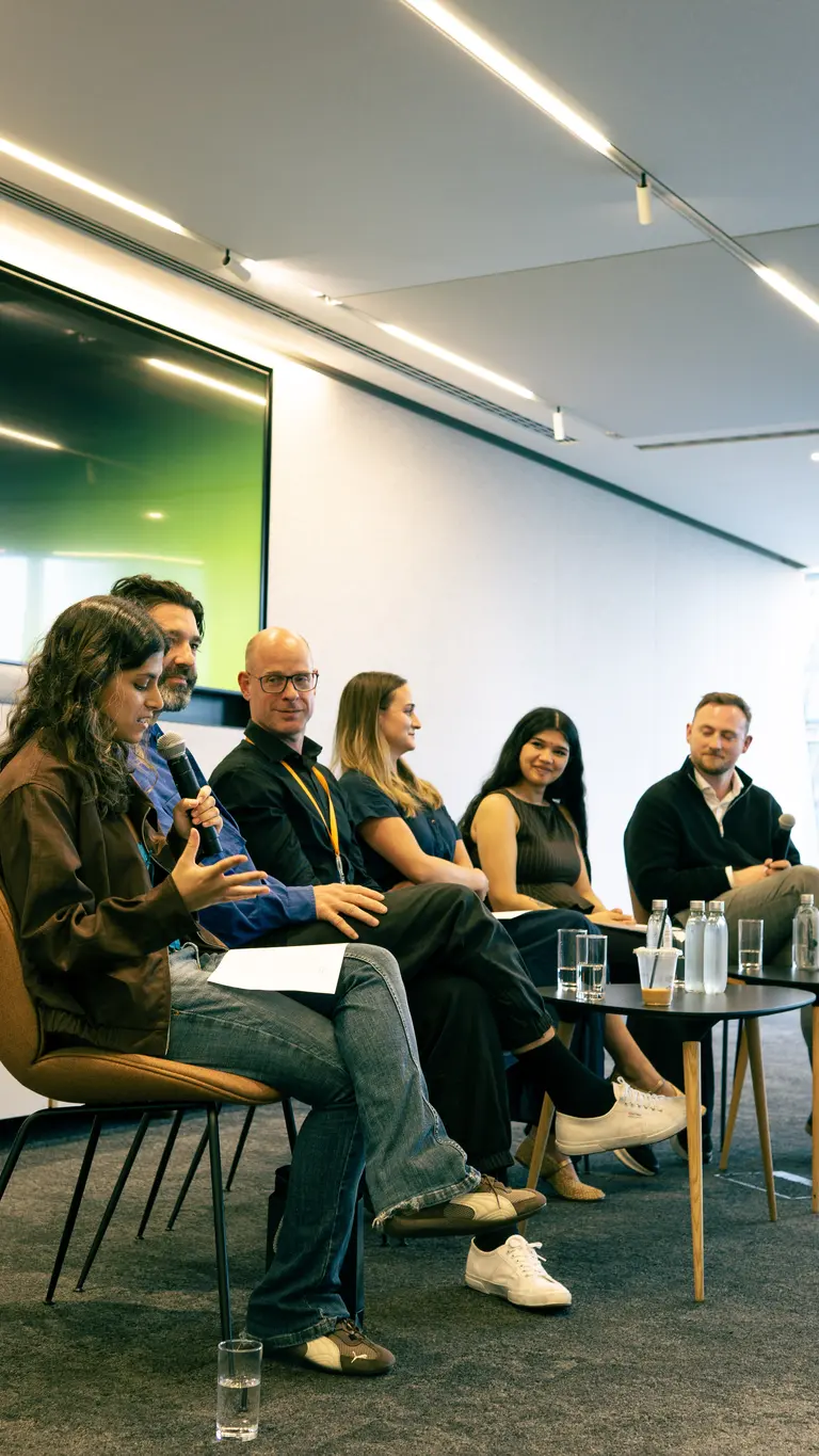 a young woman speaks into a microphone while other panel members look towards her