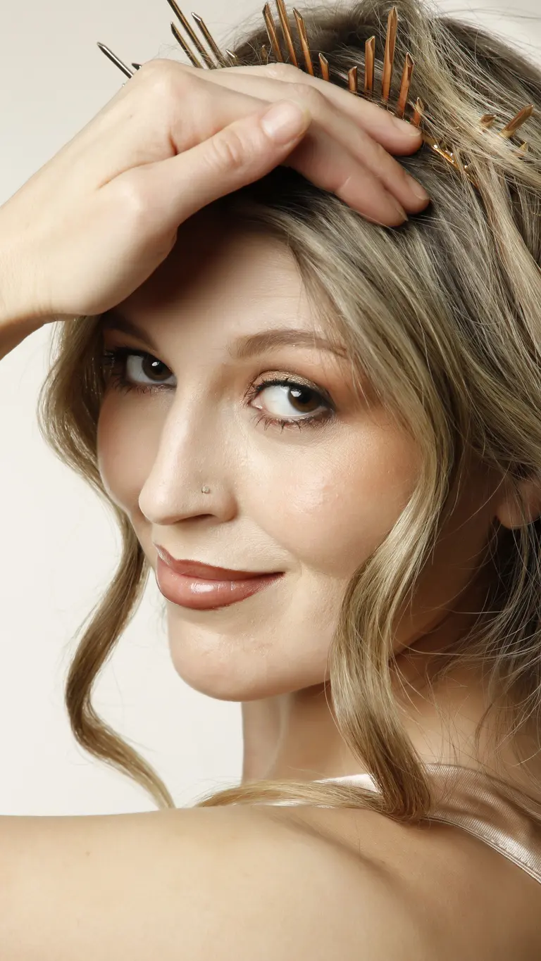 a woman with blonde wavy hair looks over her shoulder