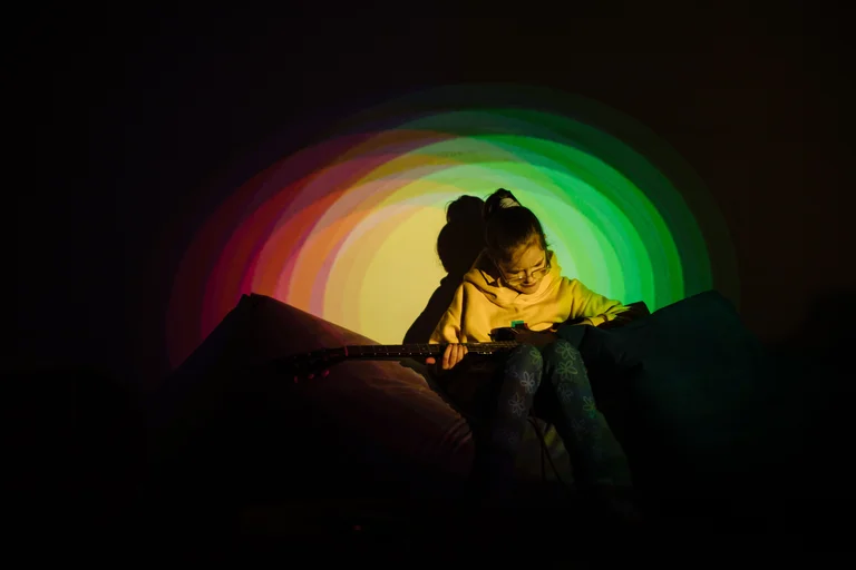 Image of young person lit by a circle of green and yellow lights interacting with multisensory equiptment.