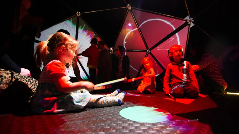 Children sat inside Soundplay's multi-sensory dome, lit by orange lights, playing with instruments. 