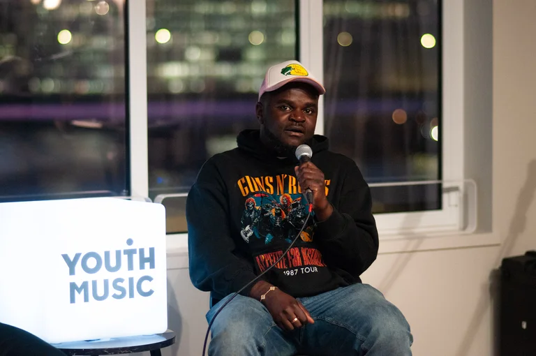 a man wearing a hoodie and cap speaks into a microphone on a panel