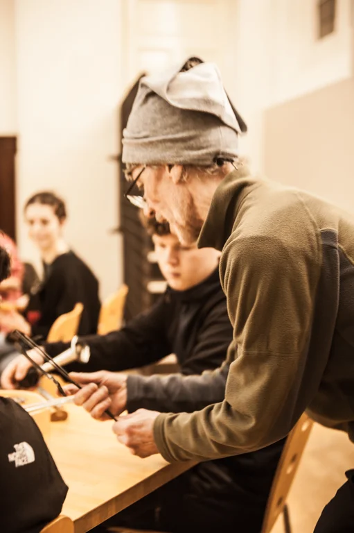 a man wearing a grey hat and glasses teaches young people in a classroom