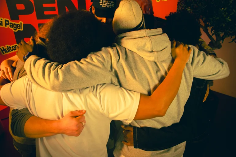 Image of a group of young people from behind with their arms around each other's shoulders