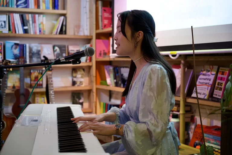 monica wat sits at a keyboard and sings into a mic