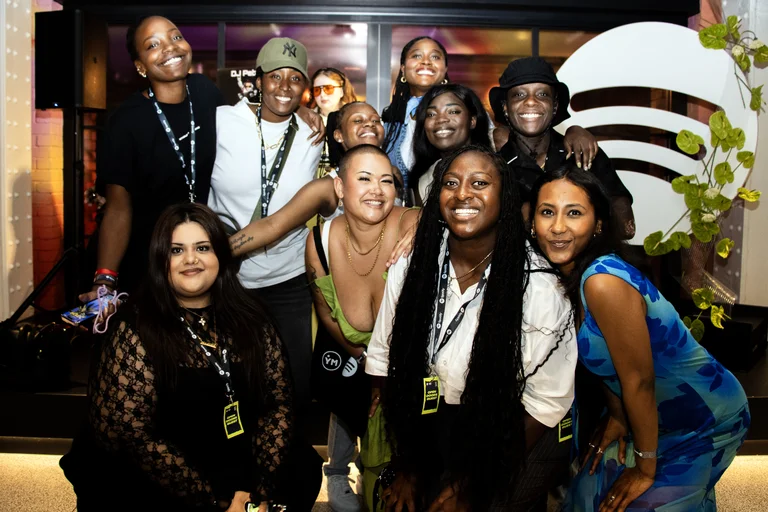 Image of people smiling and posing in front of the spotify logo