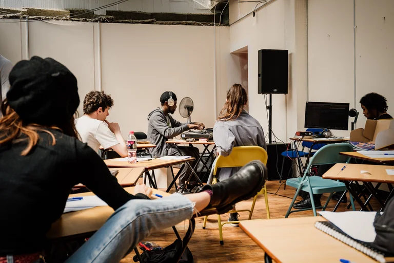 a classroom of young people watching someone using electronics