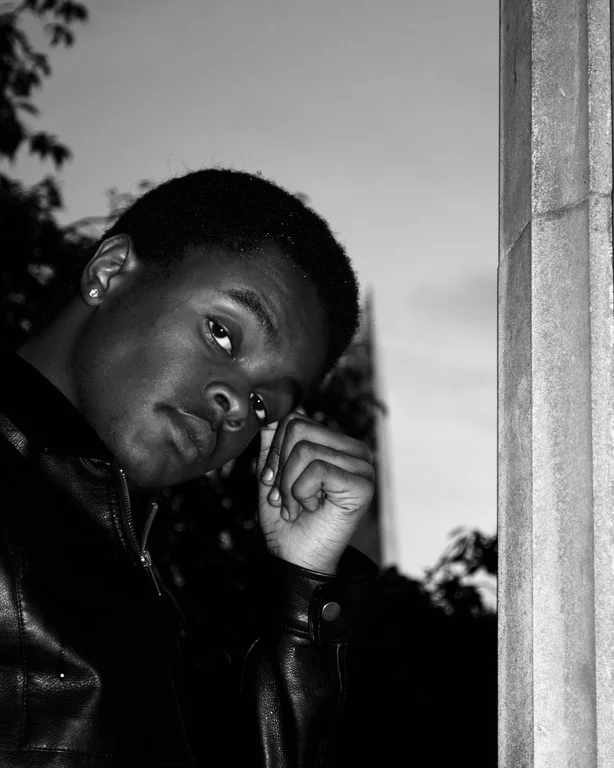 Image of Kasim, black and white, hand to his head, looking at the camera