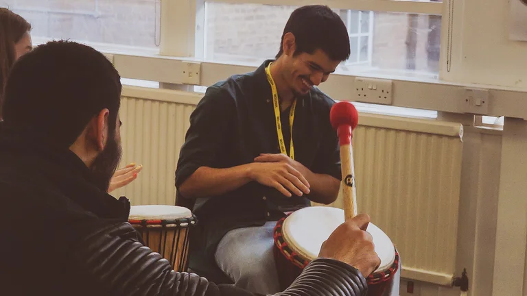 a young man laughs in a group and holds a drum between his legs