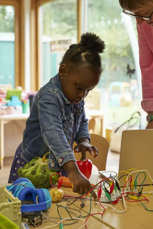 An early years child making a sculpture out of different coloured wire, while a project leader helps