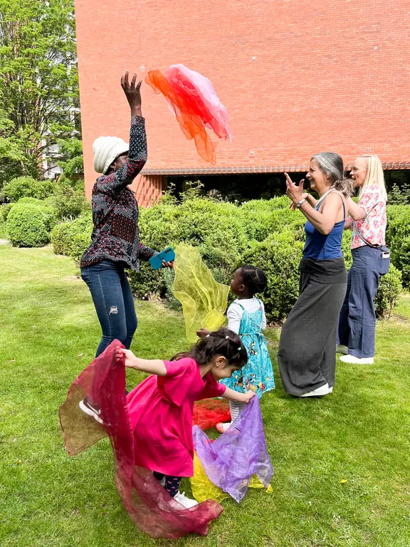 Two early years children and 3 adults, playing outsides with coloured material and dancing