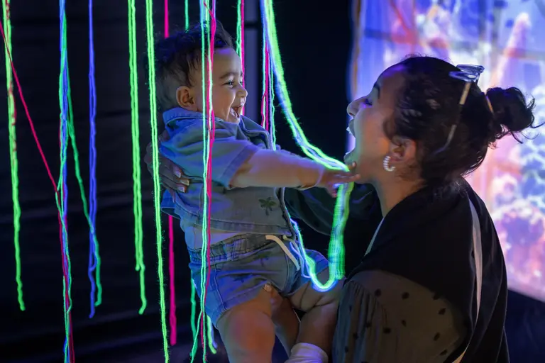 A child and their trusted adult play amongst luminous string and laugh