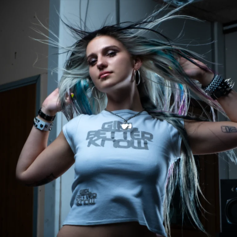 coupdekat with her hair flicked up by her hands in a dynamic manner, looking down at the camera, in an industrial background wearing a white top