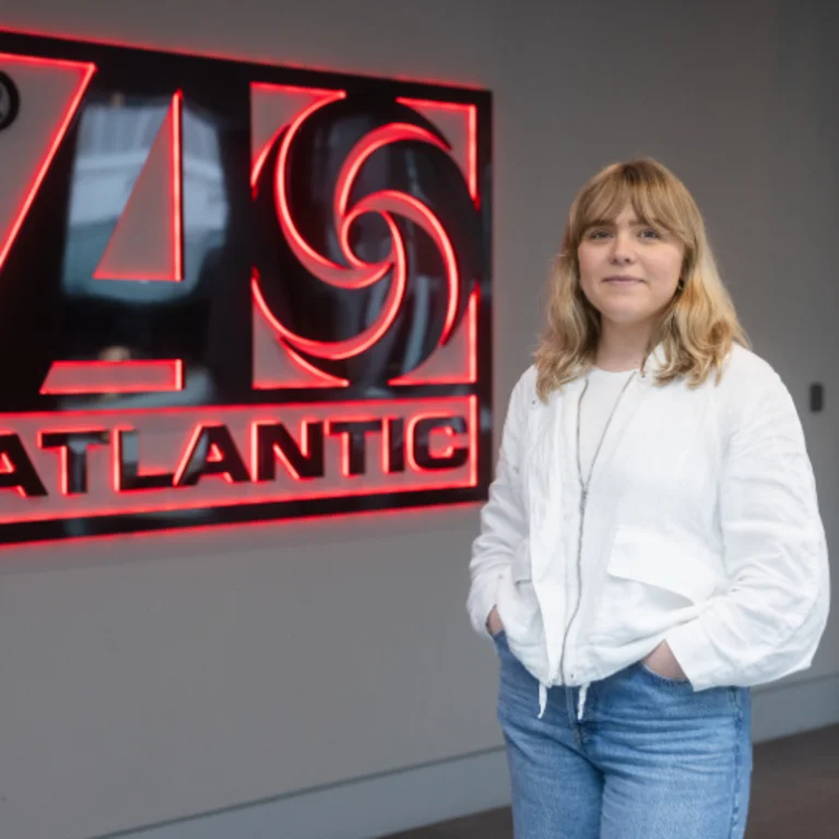 Lucy Bridge standing in front of the Atlantic sign, white shirt with hands tucked in blue jean pockets