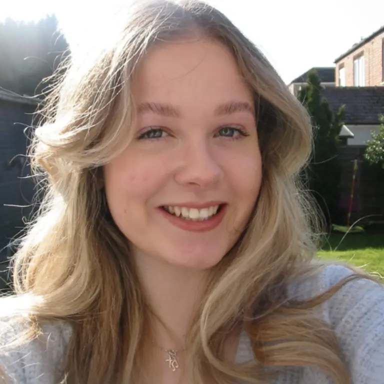 Madelaine selfie in a sunny garden, smiling with wavy blonde hair and a grey top