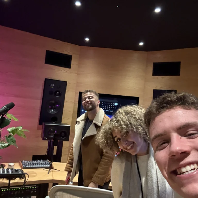 all 3 members smiling for a selfie, inside a recording studio, Hulton is holding the camera
