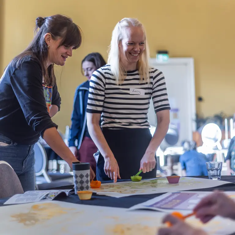 two women standing and smiling while painting and drawing on a poster