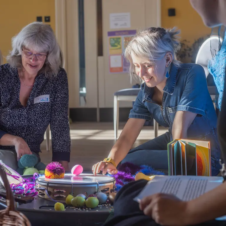two women on their knees playing with musical instruments on toys laid out on blue sheets