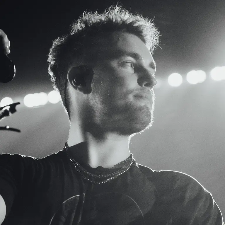 sam fender holds a microphone stand and looks to the left 