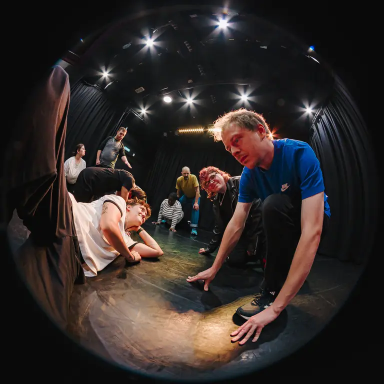 Actors on stage, on the ground or on their hands and knees, seen through a fish-eye lens affect