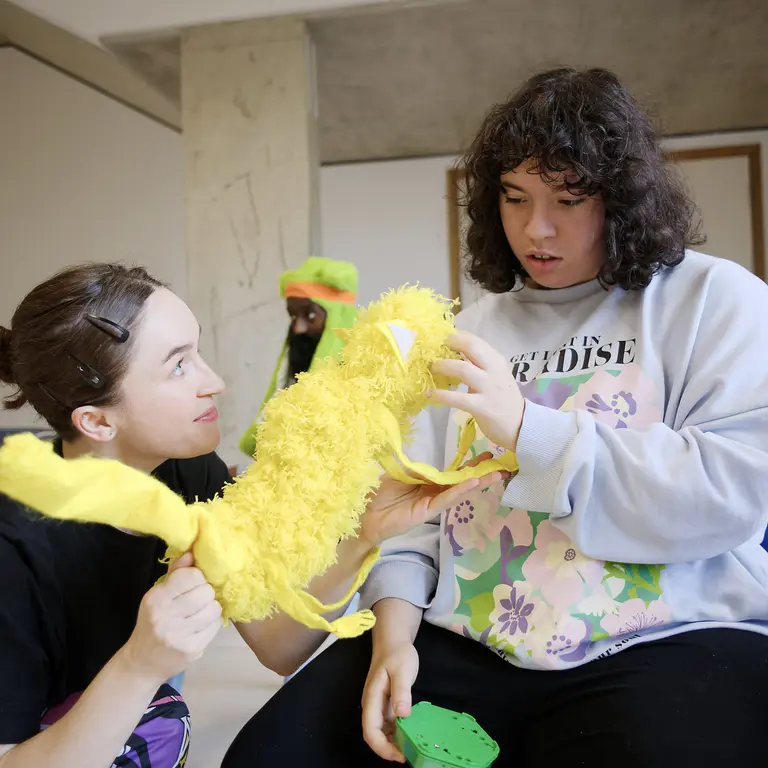 Two participants in a BLINK Dance Theatre session sit together, holding and examining a bright yellow prop during a creative movement activity in a studio space.