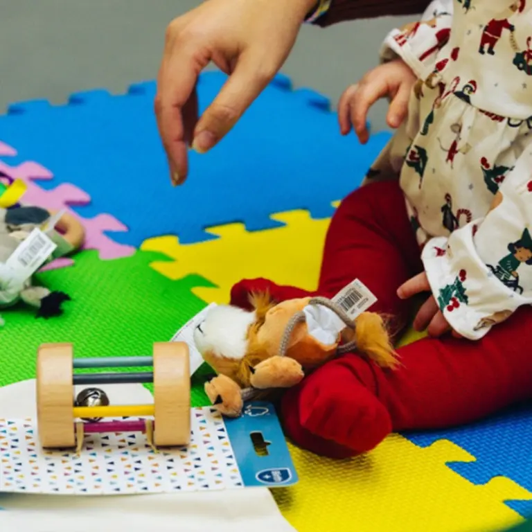 toys for children with an adult hand reaching to pick one up, child's legs in front
