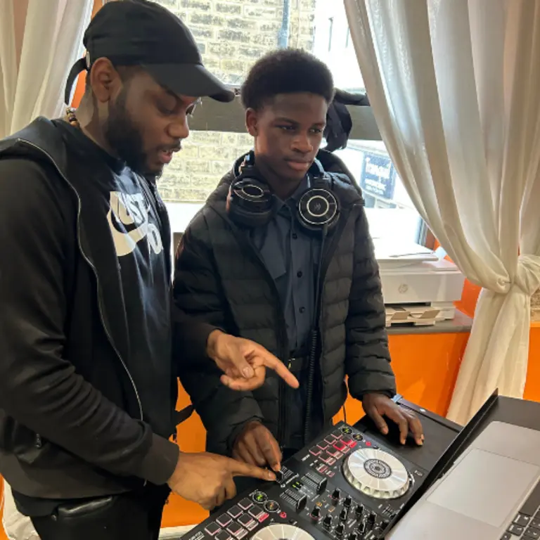 practitioner teaching a young person how to DJ in front of decks