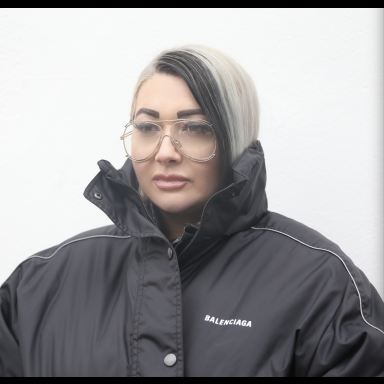Woman with black and white hair and glasses wears black coat