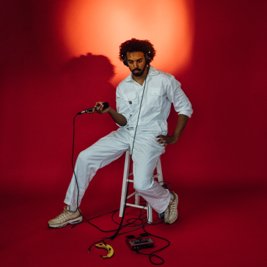 a person in a white jumpsuit sits on a stool and holds a microphone. there is a banana on the floor.